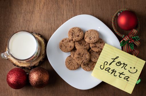 A closeup shot of a "for Santa" card on tasty cookies, milk, and Christmas decorations