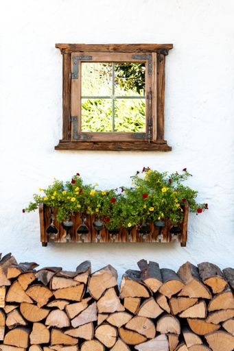 A vertical shot of a decorative window on a house wall over a flower box and firewood