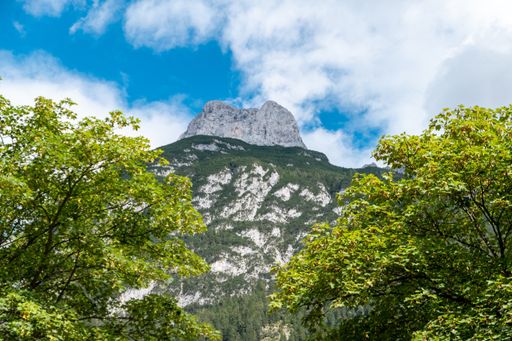 a low angle shot of the view through two trees to a mountain with a blue sky and clouds in Mittenwald in Bavaria