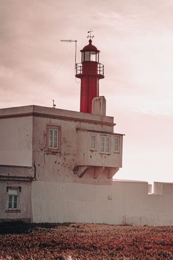 A vertical shot of a lighthouse in Portugal at sunset with a pink sky in the background