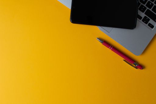 A top view of a laptop and cellphone on a yellow background