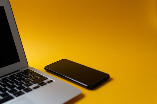 A top view of a laptop and cellphone on a yellow background