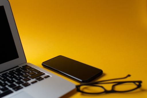 A top view of a laptop and cellphone on a yellow background