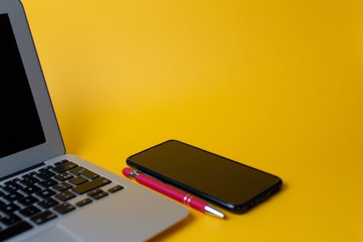 A top view of a laptop and cellphone on a yellow background