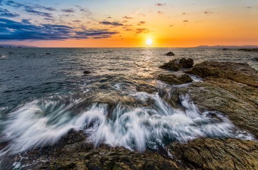 A long exposure shot of the foamy sea waves hitting the rocks with a golden sunset in the background