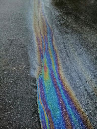 A closeup vertical shot of colorful gasoline fuel stain on asphalt pavement for abstract background
