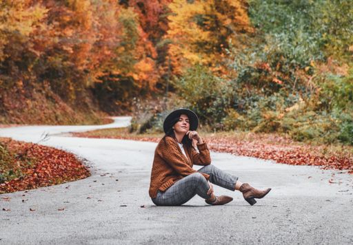 A closeup shot of an attractive young lady sitting on the road in an autumn park