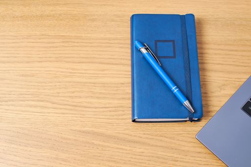 A closeup shot of a pen on a journal and laptop on a wooden table