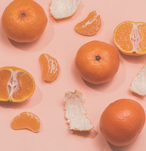 A top view of fresh tangerines halved and peels on a pink surface