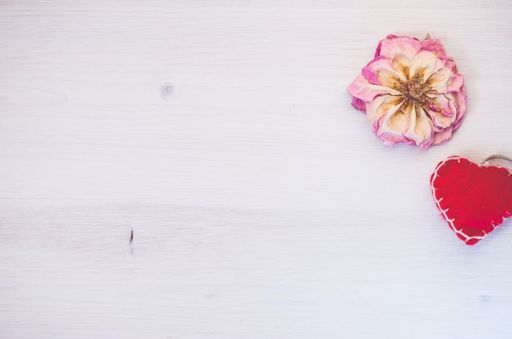 An overhead shot of withered rose blossom and handcrafted heart on a bright wood surface with space for your text