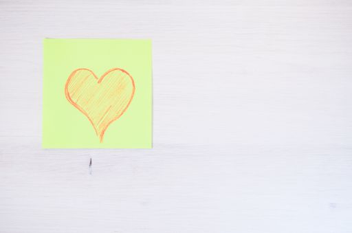 An overhead shot of a hand drawn heart on a yellow notepad on a white wooden surface - abstract backgrounds - copy space