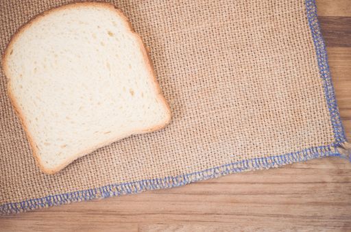 A flat lay of a slice of white bread on burlap on a wooden table with space for your text