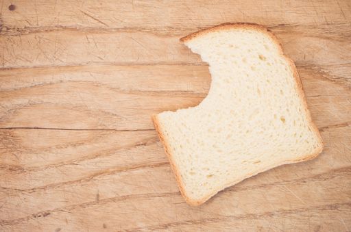 A flat lay of a slice of bitten white bread on a wooden table with space for your text