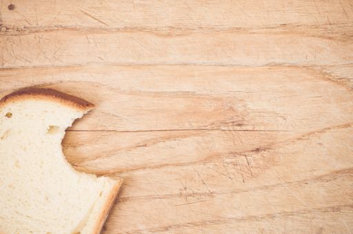 A flat lay of a slice of bitten white bread on a wooden table with space for your text