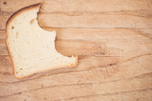 A flat lay of a slice of bitten white bread on a wooden table with space for your text