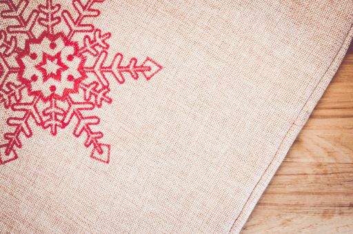 An overhead shot of a burlap cloth decorated with a sewed red snowflake