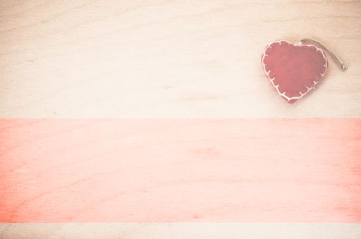 An overhead shot of hand made red felt heart decoration on a natural wood background