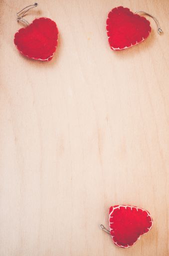 A vertical shot of hand made red felt heart decorations on a natural wood background