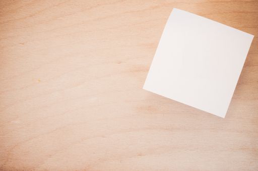 An overhead shot of a white blank sticky note on a wood textured surface with space for your text