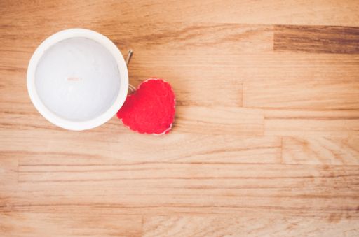 An overhead shot of a felt heart and white candle on a natural wood surface - copy space