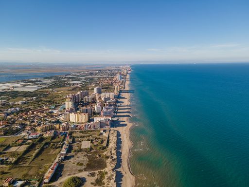 An aerial shot of a long sandy beach and buildings on a sunny day near Valencia, Spain