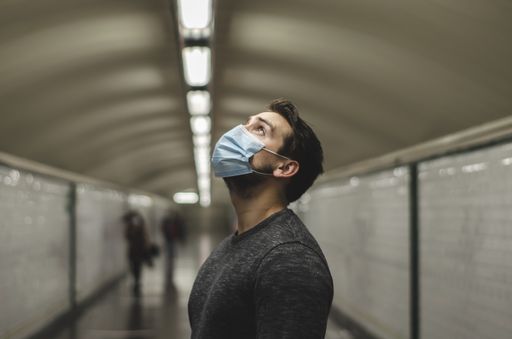 A young Caucasian man wearing a face mask looking up in a subway tunnel - new normal concept