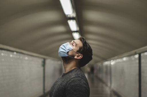 A young Caucasian man wearing a face mask with eyes closed in a subway tunnel - new normal concept