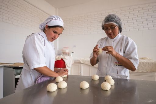 Sucre, Bolivia - August 3 2013: Two Brown Women with Indigenous Features are Using a White Food Uniform and is Making Bread with Flour Dough