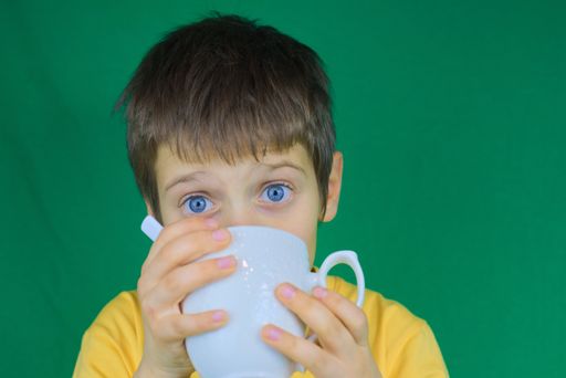 A closeup shot of a cute boy drinking a cup of juice and looking at the camera