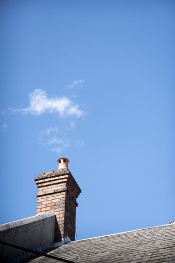 A vertical shot of a building chimney with clouds like smoke