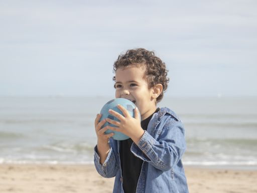 A cheerful little boy in boots playing on the sandy seashore