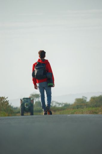 A vertical shot of a young man with a backpack walking on the road