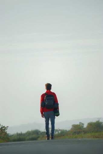 A vertical shot of a young man with a backpack standing on the road