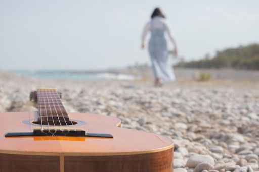 A closeup shot of a brown guitar on a rocky beach with a walking female
