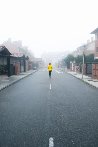A vertical shot of a woman walking in the middle of a foggy street wearing a yellow down jacket