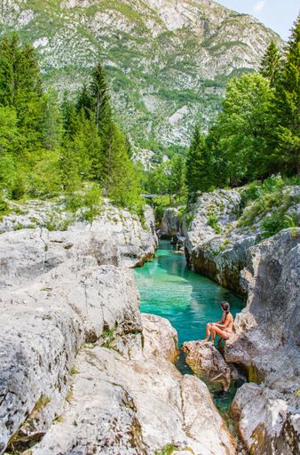 Beautiful gorge with emerald river, Soca river valley, Slovenia. Woman sitting on edge of gorge, swimming, swimwear.