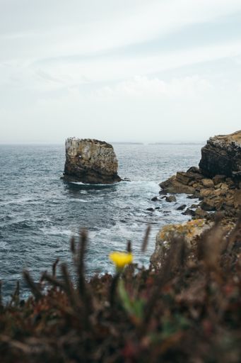 A vertical shot of an immense rock formation with a wavy seascape view in Peniche, Portugal