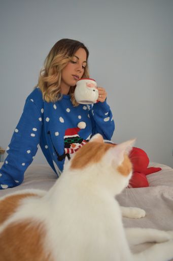 A female drinking morning coffee on a cozy bed with a cat in the foreground