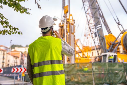 A technician engineer observing the team of workers at the construction site while having a phone call