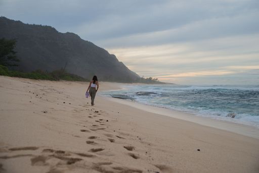 A back view of a female walking on a sandy beach on a cloudy day