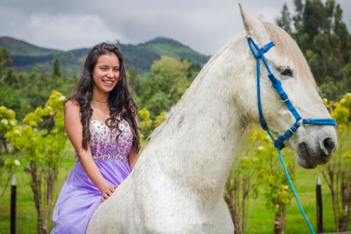 A shallow focus of a happy young female in a purple dress riding a white horse in a field