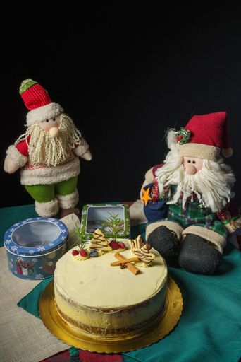 A Christmas cake, gift boxes and stuffed Santa toys on a table on a black background
