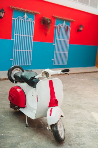 A vertical shot of a vintage Vespa scooter parked in front of a red and blue wall