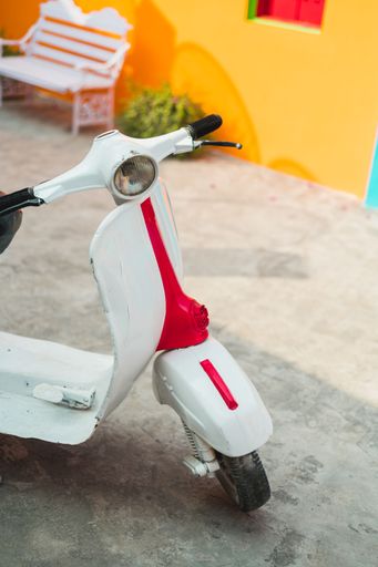 A vertical shot of a vintage Vespa scooter parked in front of a yellow wall