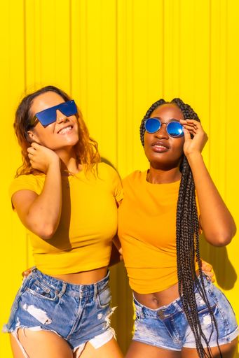 A vertical shot of two friends posing by a yellow wall