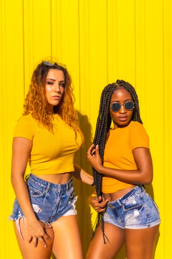 A vertical shot of two friends posing by a yellow wall