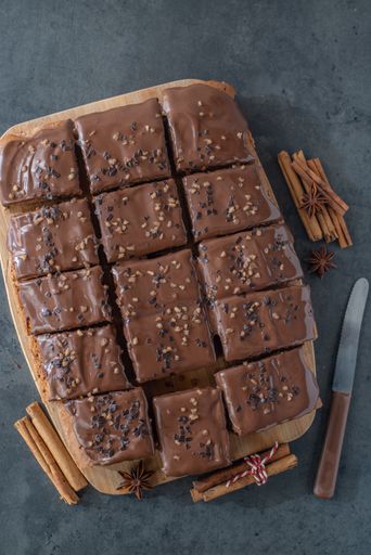 A vertical top view of gingerbread chocolate brownies on wooden board with cinnamon near it