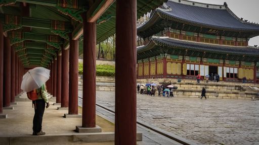 A person with an umbrella and a backpack standing near Injeongjeon Hall in South Korea