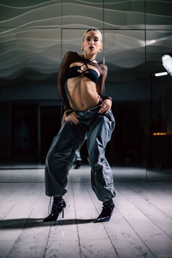 A vertical shot of a beautiful female dancer posing in mesh overlay crop top in black and baggy pants