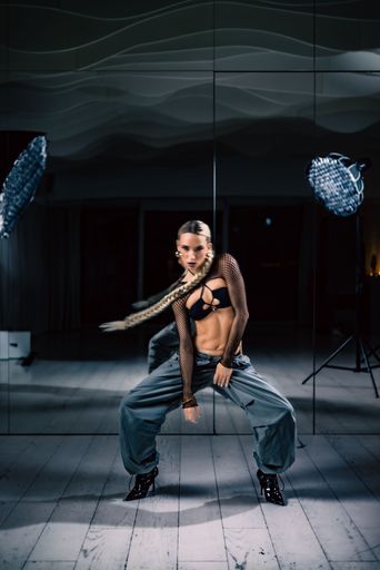 A vertical shot of a beautiful female dancer posing in mesh overlay crop top in black and baggy pants